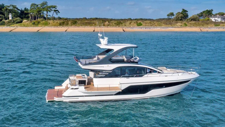 Luxury yacht cruising on blue waters with a scenic shoreline and trees in the background under a clear sky.